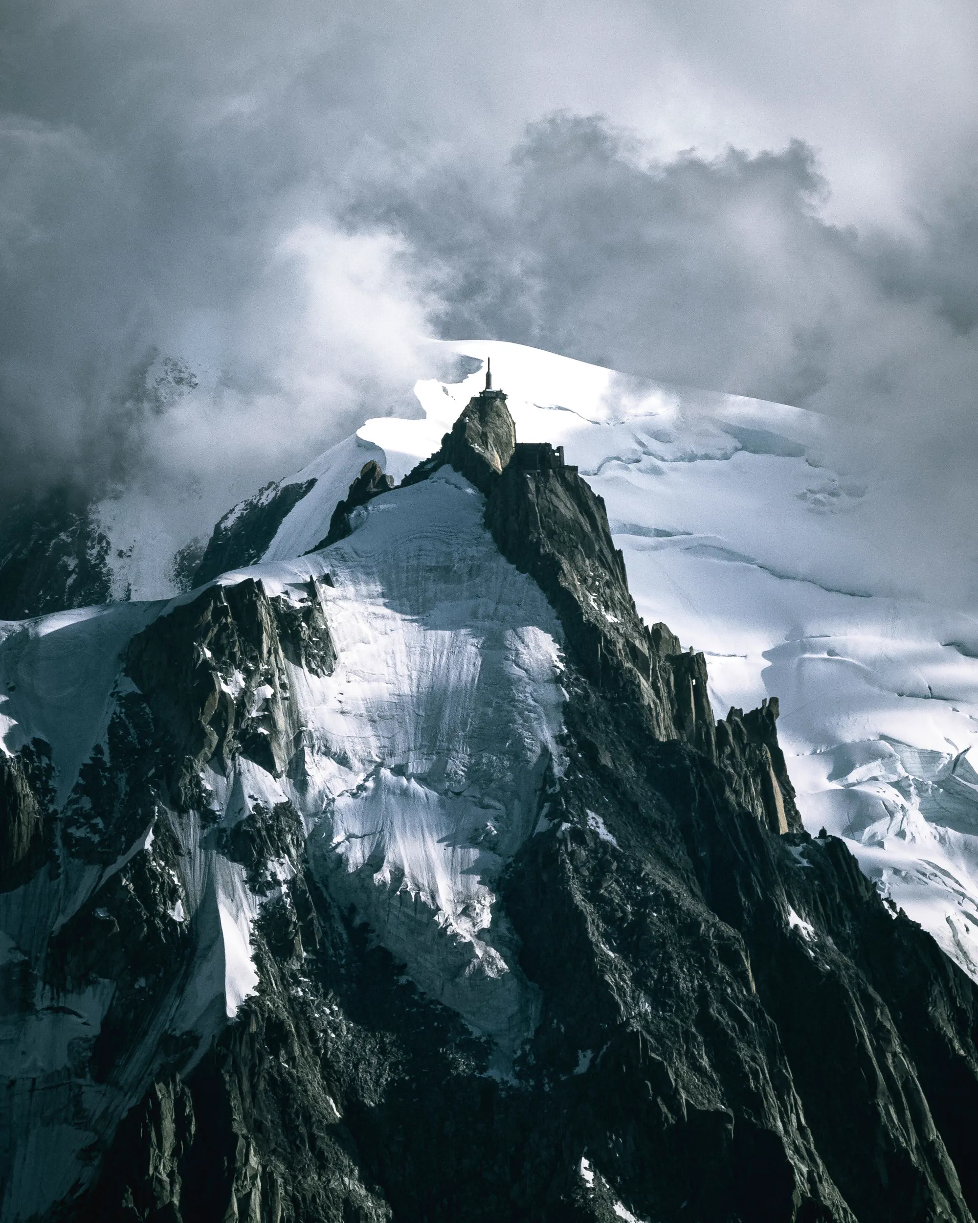 A dark, jagged mountain peak rising into a bank of low cloud.