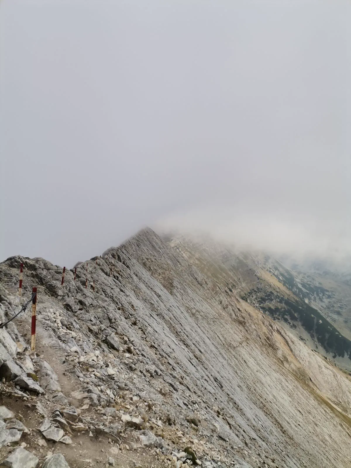 A hiker on a grassy mountain ridge with high peaks beyond.